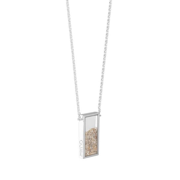 A rectangular silver pendant with a free flowing mix of sand behind sapphire glass from side showing inscription OUAW