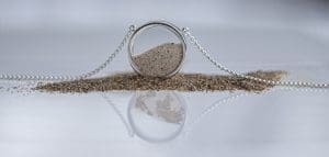 A silver necklace with sand and its reflection showing a world map