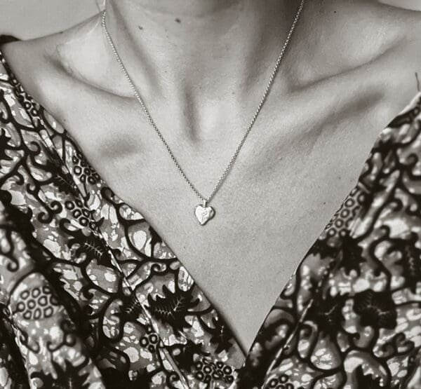 Woman wearing a heart shaped necklace shaped after a grain of sand